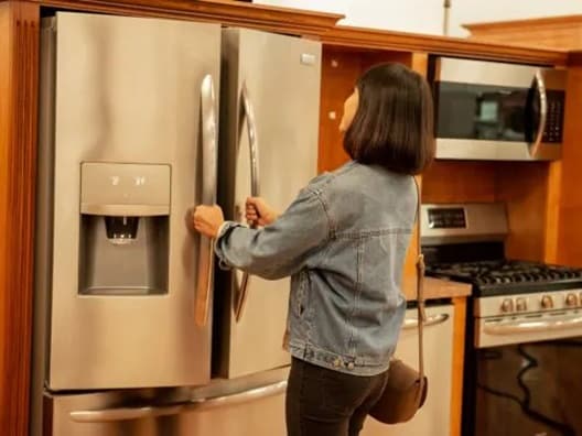 A women opening a French door refrigerator while holding both of its handles.