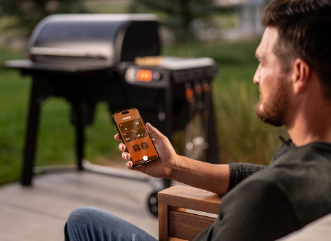 Traeger Barbeque model TFB86MLH, man sitting outside pointing his smart phone toward the barbeque