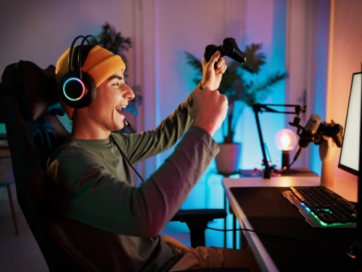 Teenage boy sitting on his gaming chair wearing his computer headset, fists pumped in the air