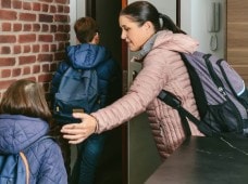 Woman herding two children out the door, all three wearing backpacks