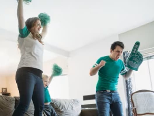 A family of three jumping around with a foam finger and pom poms.
