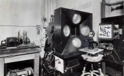 Black and white photo of early TV studio featuring an old TV camera, a Felix the Cat doll, and an early NBC logo