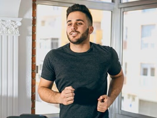 A man jogging in a room in front of windows.