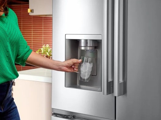 Woman's arm holding a glass full of ice that was dispensed from a stainless steel French door refrigerator.