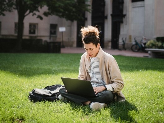 College Student sitting on lawn looking at laptop