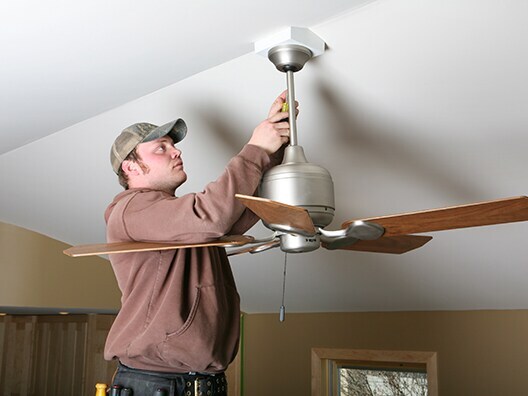Guy in baseball cap on ladder fixing ceiling fan