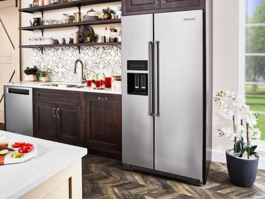 Stainless side-by-side fridge in kitchen amongst dark brown wooden cabinetry