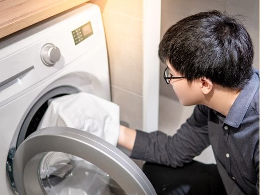 Guy with black hair, gray shirt, and glasses loading a shower curtain into a washer